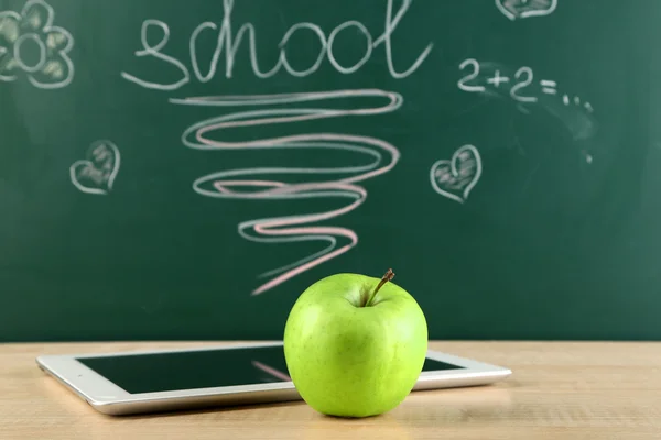 Tableta digital y manzana en el escritorio frente a la pizarra —  Fotos de Stock