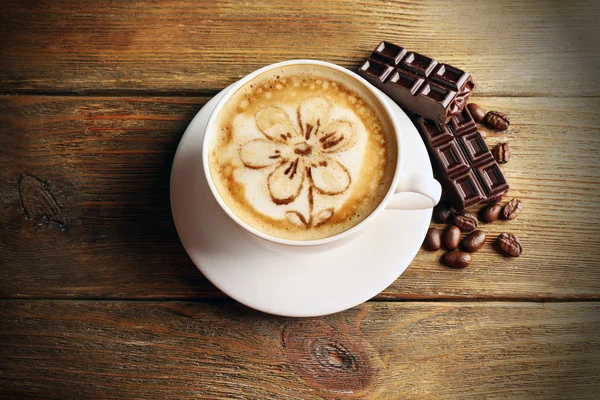 Cup of coffee latte art with grains and chocolate on wooden background — Stock Photo, Image