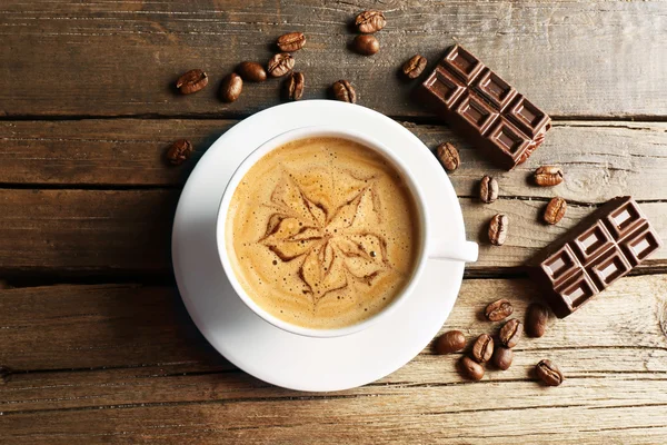 Cup of coffee latte art with grains and chocolate on wooden table, top view — Stock Photo, Image