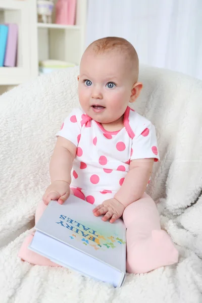 Menina bonito sentado em cadeira de braço com livro, em casa fundo interior — Fotografia de Stock