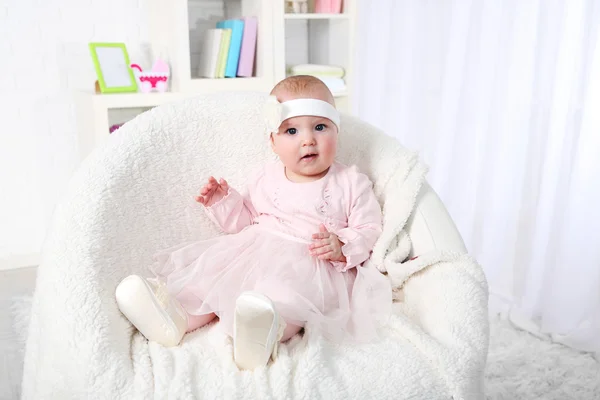 Linda niña en vestido rosa sentado en el sillón, en el fondo interior del hogar —  Fotos de Stock