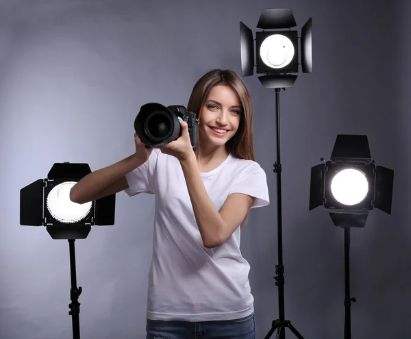 Young female photographer taking photos on grey background