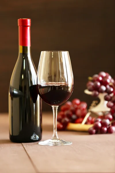 Bottle and glass of wine with grape on wooden table on dark background Stock Image