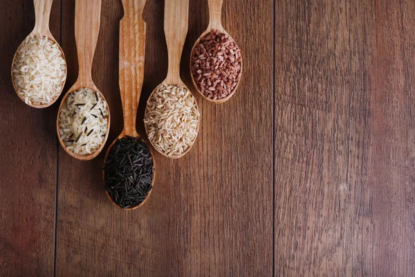 Diferentes tipos de arroz en cucharas sobre fondo de madera — Foto de Stock