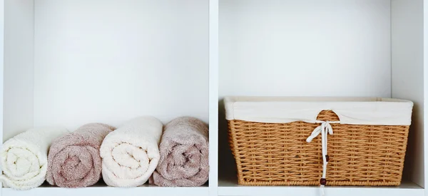 Rullade handdukar med rotting korg på hyllan av rack bakgrund — Stockfoto