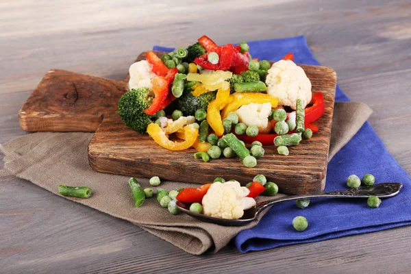 Verduras congeladas sobre tabla de cortar, sobre servilleta, sobre fondo de mesa de madera —  Fotos de Stock