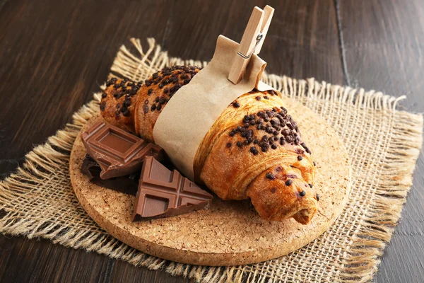 Croissant fresco e gustoso con cioccolato a bordo, su fondo legno — Foto Stock