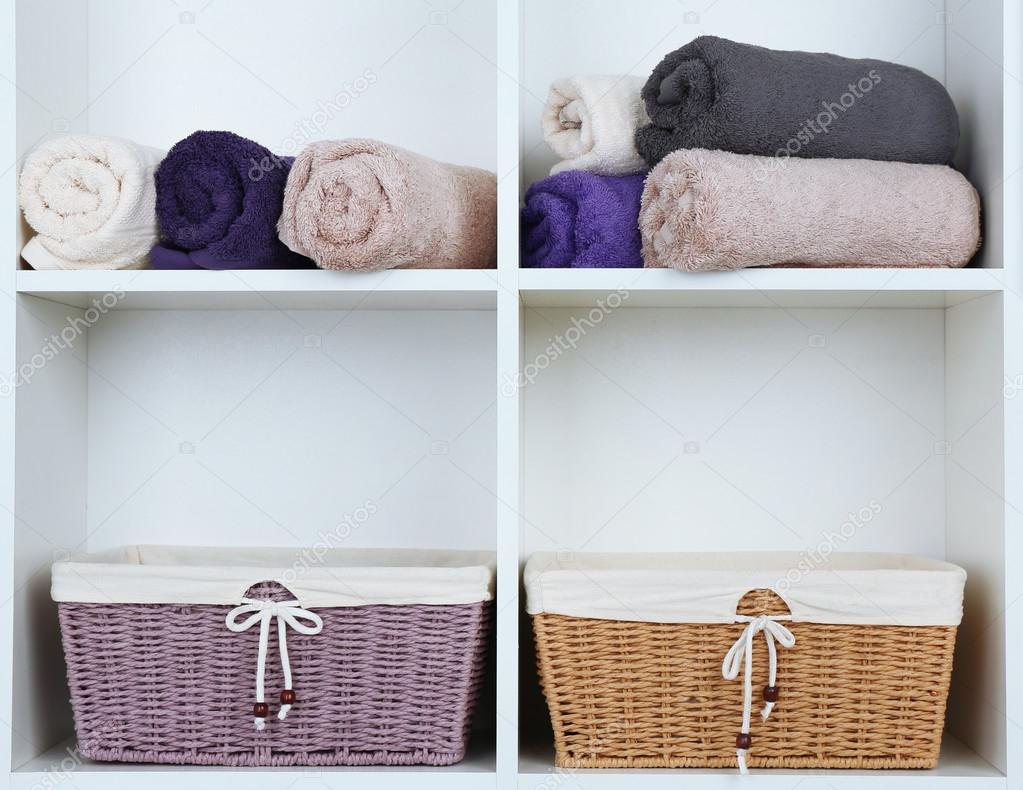 Rolled towels with wicker baskets on shelf of rack background