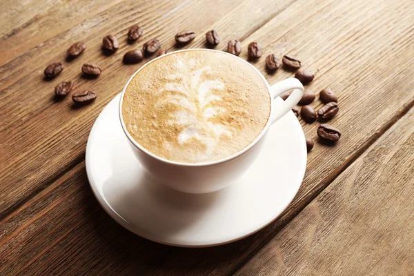 Cup of latte art coffee with grains on wooden background — Stock Photo, Image