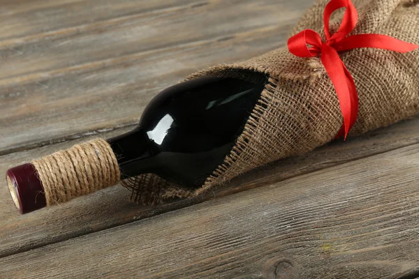 Бутылка красного вина, завернутая в мешковину на фоне деревянных досок — стоковое фото