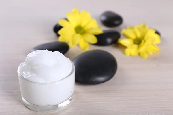 Creme cosmético com flores e pedras de spa em fundo de madeira — Fotografia de Stock