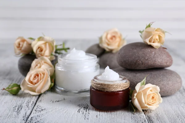 Crema cosmética con flores y piedras de spa sobre fondo de madera — Foto de Stock