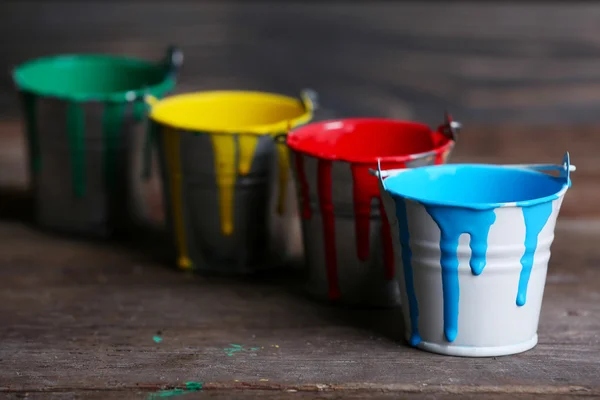 Metal buckets with colorful paint on wooden background — Stock Photo, Image