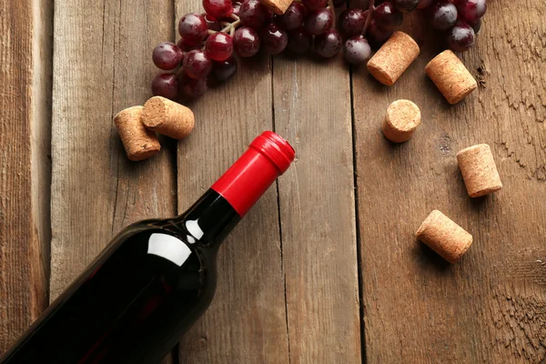 Glass bottle of wine with corks and grapes on wooden table background — Stock Photo, Image