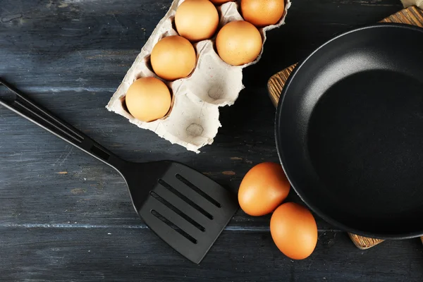 Still life with eggs and pan on wooden table, top view — Stock Photo, Image