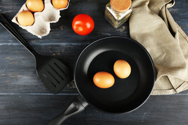 Still life with eggs and pan on wooden table, top view
