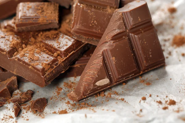 Pieces of chocolate with cocoa on parchment, closeup — Stock Photo, Image