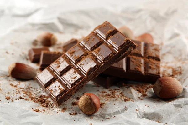 Pieces of chocolate with cocoa on parchment, closeup — Stock Photo, Image