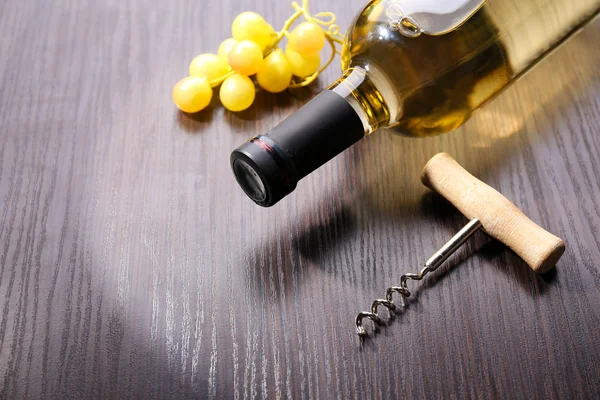 Láhev vína z hroznů a vývrtka na dřevěné pozadí — Stock fotografie