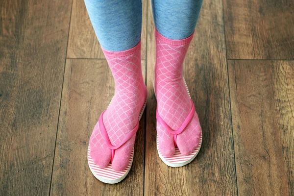 Female feet in socks with pink flip-flops, on floor background — Stock Photo, Image