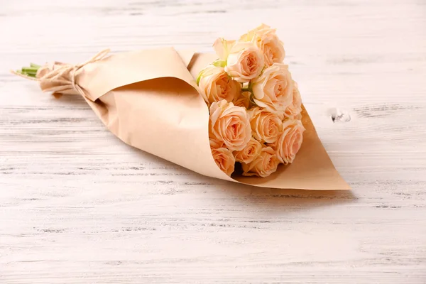 Bouquet of fresh roses wrapped in paper on wooden background — Stock Photo, Image