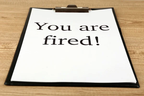 Сообщение You 're Fired on clipboard on wooden table, closeup — стоковое фото