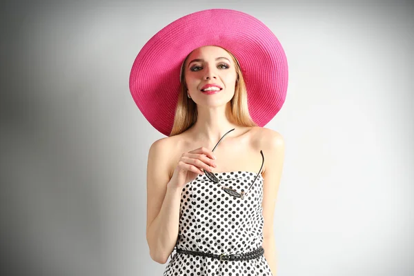 A rózsaszín kalapot, napszemüveget, szürke háttér kifejező fiatal modell — Stock Fotó