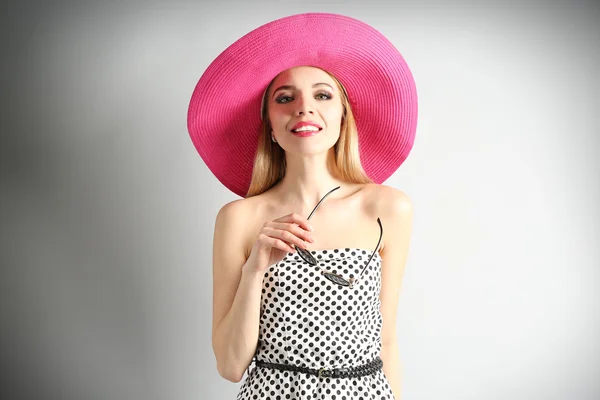 Modelo joven expresivo en sombrero rosa con gafas de sol sobre fondo gris — Foto de Stock