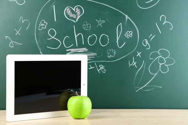 Digital tablet and apple on  desk in front of blackboard — Stock Photo, Image