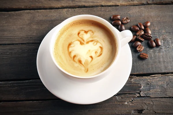 Xícara de café arte latte com grãos em fundo de madeira — Fotografia de Stock