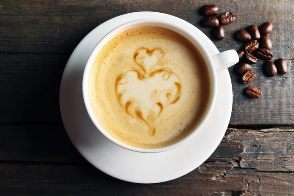 Tasse de café latte art avec des grains sur fond en bois — Photo