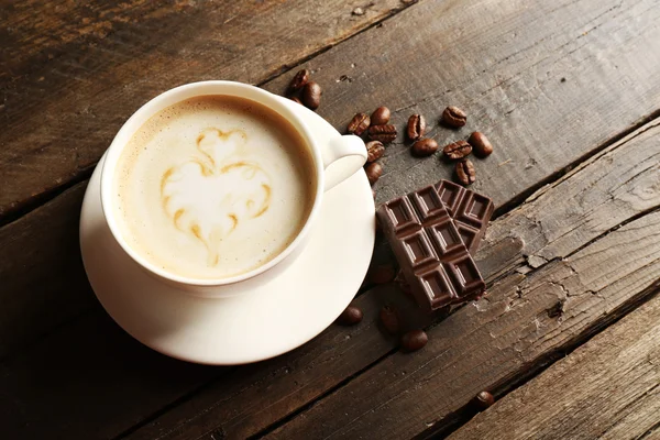 Taza de café latte arte con granos y chocolate sobre fondo de madera —  Fotos de Stock