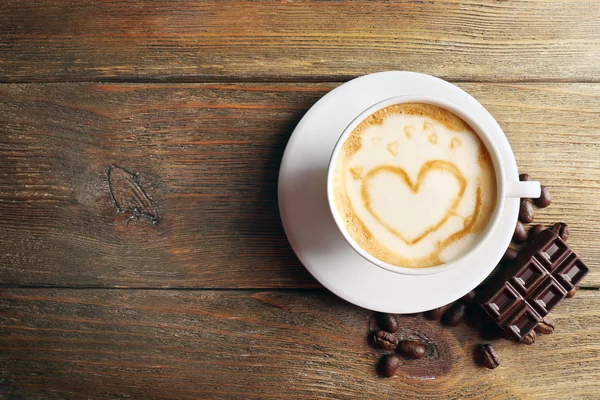 Xícara de café arte latte com grãos e chocolate na mesa de madeira, vista superior — Fotografia de Stock