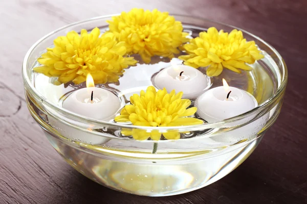 Bowl of spa water with flowers and candles on wooden table, closeup