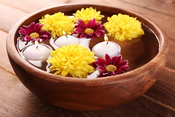 Tigela de água termal com flores e velas em mesa de madeira, close-up — Fotografia de Stock