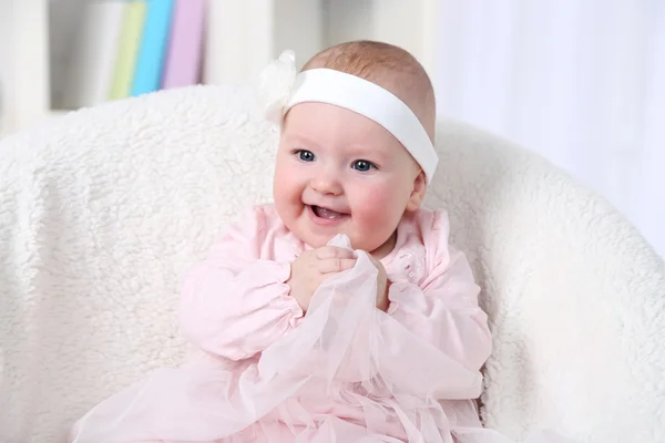 Cute baby girl in pink dress sitting in arm-chair, on home interior background — Stock Photo, Image