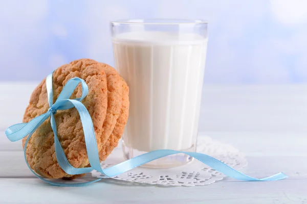 Sabrosas galletas y vaso de leche en la mesa de madera de color, sobre fondo brillante —  Fotos de Stock