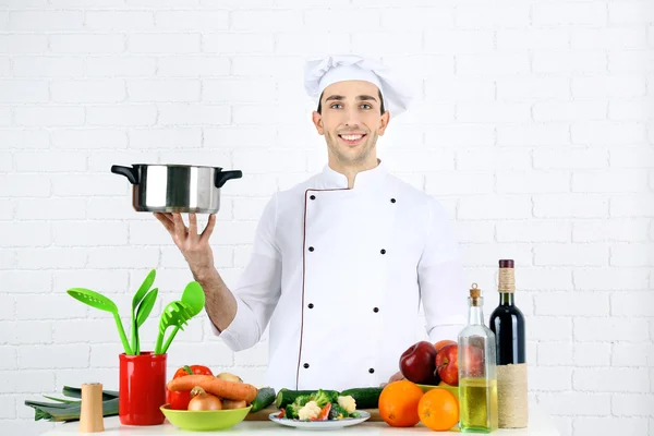 Chef en la mesa con diferentes productos y utensilios en la cocina sobre fondo blanco de la pared — Foto de Stock