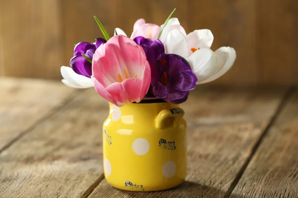 Beautiful spring flowers in yellow pot on wooden background — Stock Photo, Image