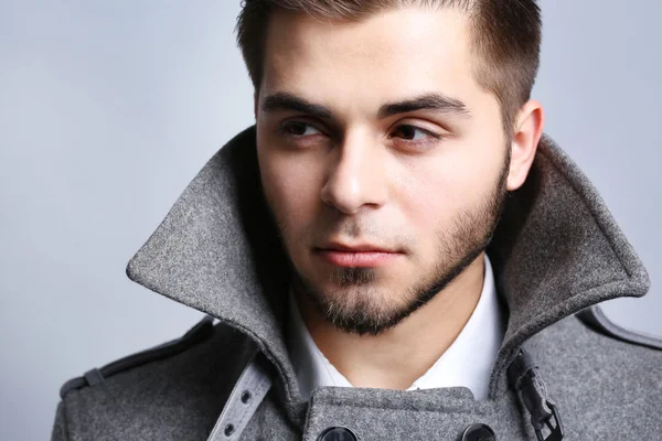 Young man in coat on gray background — Stock Photo, Image