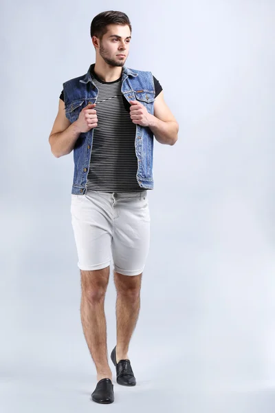 在灰色的背景上的白色短裤和牛仔裤背心的男人 — 图库照片