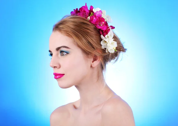 Retrato de jovem com flores no cabelo em fundo azul — Fotografia de Stock