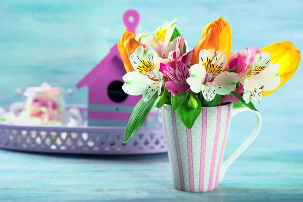 Schöne Blumen in Tasse, auf farbigem Holzhintergrund — Stockfoto