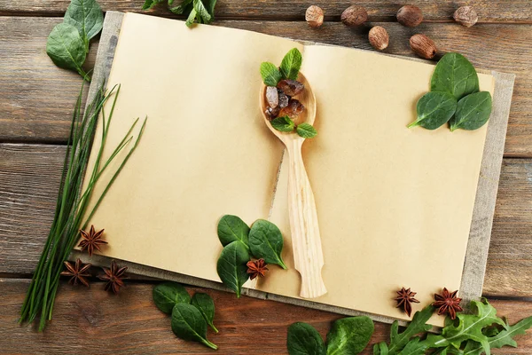 Livro de receitas aberto com ervas frescas e especiarias em fundo de madeira — Fotografia de Stock