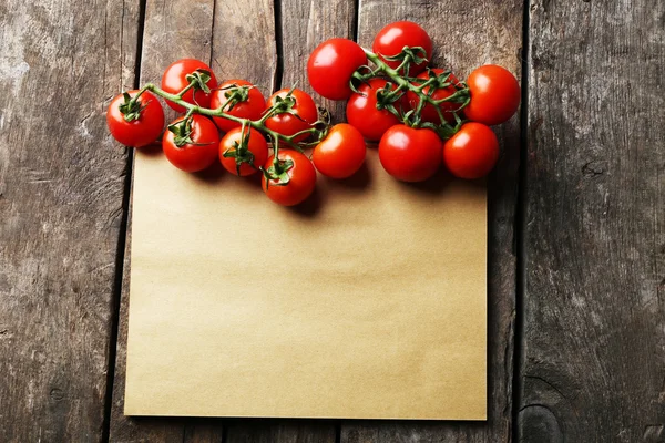 List papíru s cherry rajčátky na rustikální dřevěné povrchu pozadí — Stock fotografie