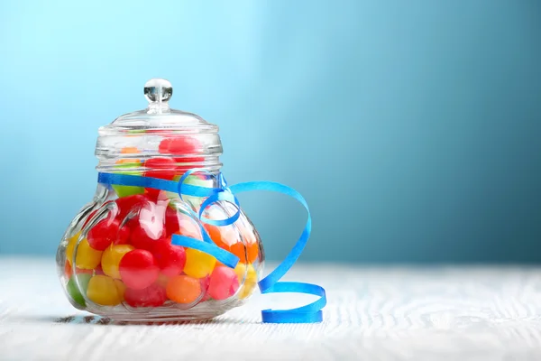 Coloridos caramelos en frasco sobre la mesa sobre fondo azul —  Fotos de Stock