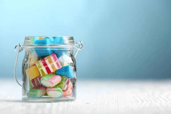 Caramelle colorate in barattolo sul tavolo su sfondo blu — Foto Stock