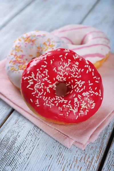 Köstliche Donuts mit Sahnehäubchen auf Serviette auf Holzgrund — Stockfoto