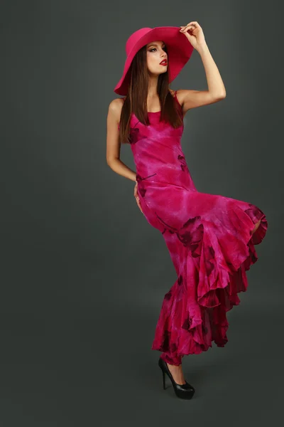 Beautiful young woman in long pink dress and hat on dark gray background — Stock Photo, Image
