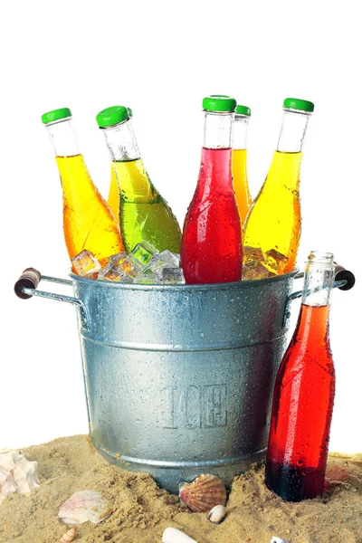 Flaschen leckeres Getränk in Metalleimer mit Eis auf Sand isoliert auf weiß — Stockfoto